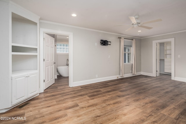 unfurnished bedroom featuring crown molding, a walk in closet, hardwood / wood-style flooring, and ceiling fan