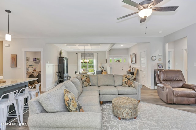 living room with hardwood / wood-style flooring, washer and dryer, and ceiling fan with notable chandelier