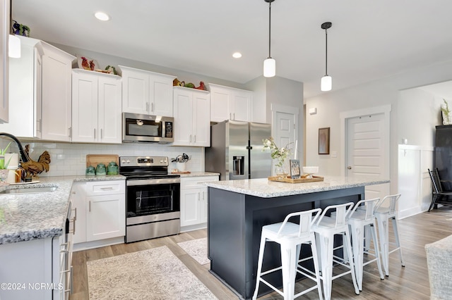 kitchen featuring pendant lighting, sink, stainless steel appliances, a center island, and white cabinets