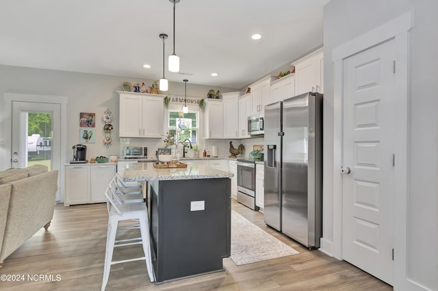 kitchen featuring appliances with stainless steel finishes, white cabinetry, hanging light fixtures, backsplash, and a center island