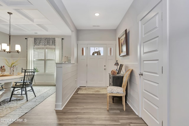 entrance foyer featuring hardwood / wood-style flooring, coffered ceiling, a chandelier, and beamed ceiling