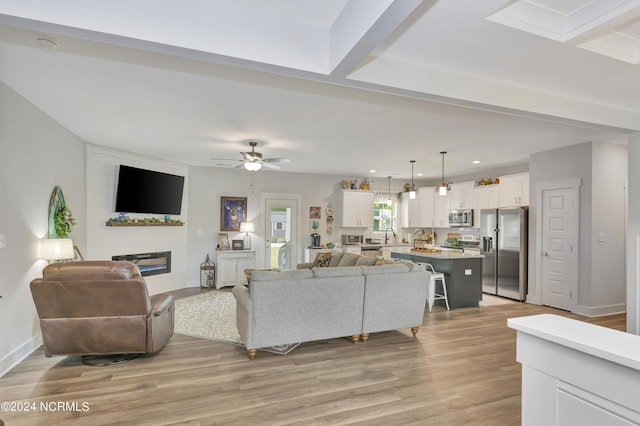 living room featuring ceiling fan, a large fireplace, sink, and light hardwood / wood-style flooring