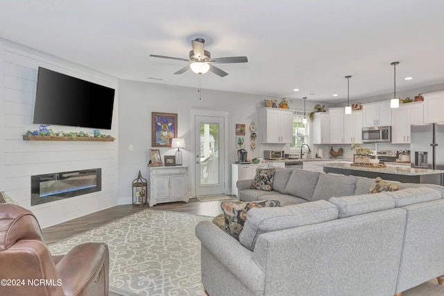 living room with hardwood / wood-style flooring, ceiling fan, sink, and a fireplace