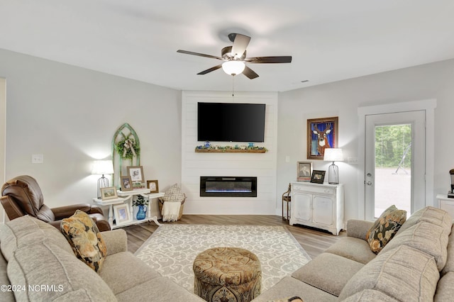 living room featuring ceiling fan, a large fireplace, and light hardwood / wood-style floors