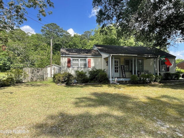 view of front of home with a porch, an outdoor structure, fence, a storage unit, and a front lawn