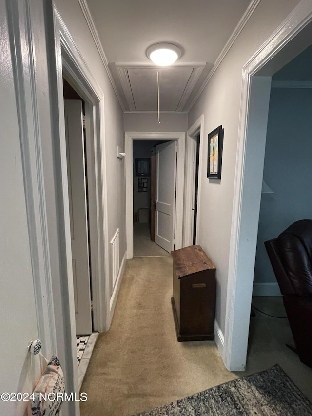 hallway with baseboards, ornamental molding, attic access, and light colored carpet