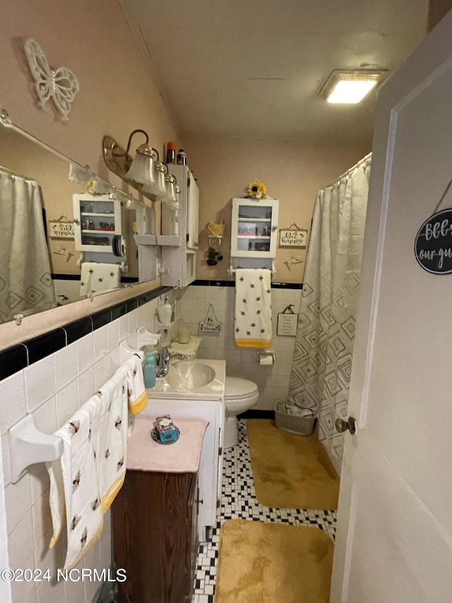 bathroom featuring toilet, a wainscoted wall, a shower with curtain, vanity, and tile walls