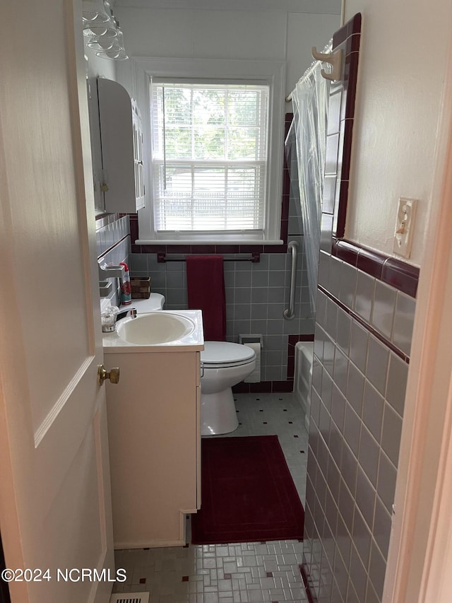 full bath featuring toilet, shower / bath combo with shower curtain, vanity, and tile walls