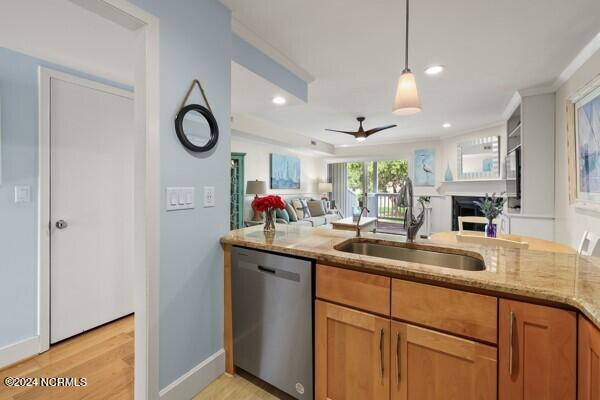 kitchen with light wood finished floors, dishwasher, open floor plan, light stone countertops, and a sink