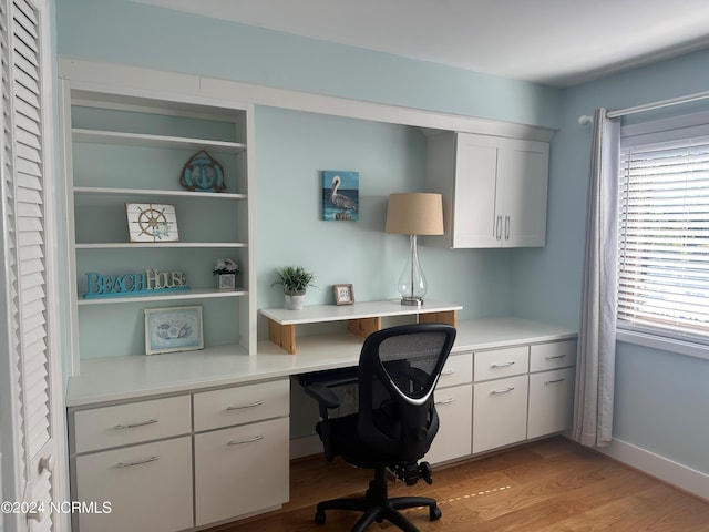 office area featuring light wood-type flooring, built in study area, and baseboards