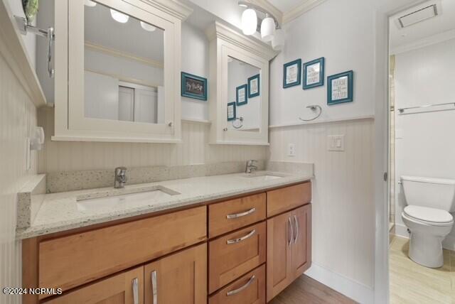 bathroom with toilet, double vanity, ornamental molding, and a sink