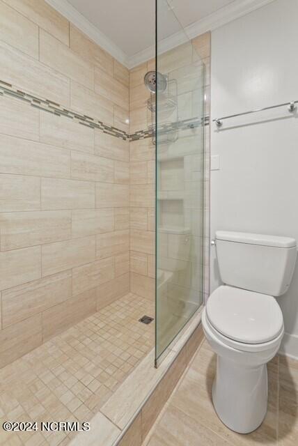 bathroom featuring toilet, crown molding, and tiled shower