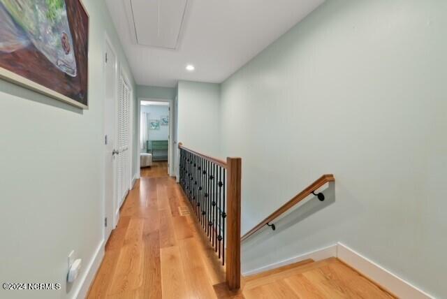 hallway featuring attic access, baseboards, light wood-style flooring, and an upstairs landing