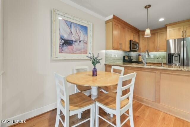 kitchen featuring baseboards, light wood-style flooring, backsplash, stainless steel appliances, and a sink