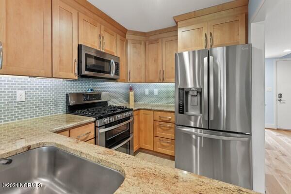 kitchen featuring appliances with stainless steel finishes, light wood-style flooring, light stone counters, and decorative backsplash