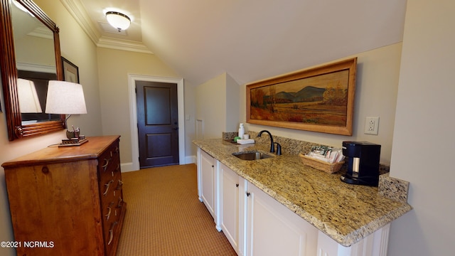 kitchen with lofted ceiling, light stone counters, a sink, white cabinets, and ornamental molding