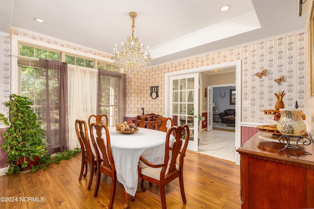 dining space featuring ornamental molding, a raised ceiling, a chandelier, and light hardwood / wood-style flooring