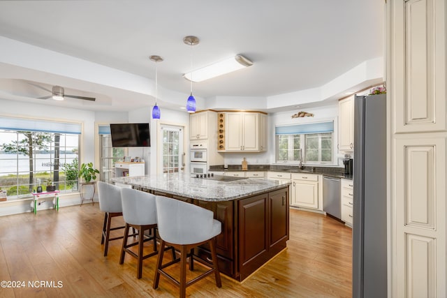 kitchen with ceiling fan, appliances with stainless steel finishes, hanging light fixtures, a kitchen island, and light stone counters