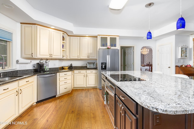 kitchen featuring appliances with stainless steel finishes, pendant lighting, a tray ceiling, and light stone countertops