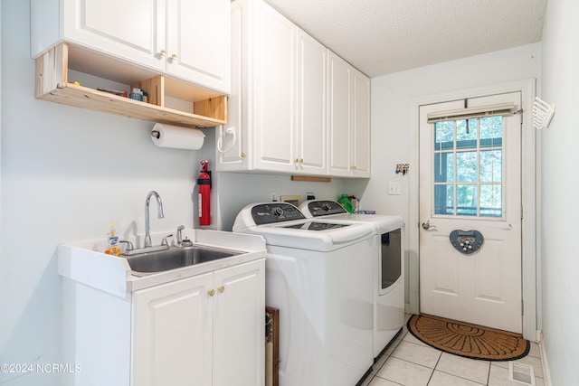 laundry room with separate washer and dryer, light tile patterned flooring, a textured ceiling, cabinets, and sink