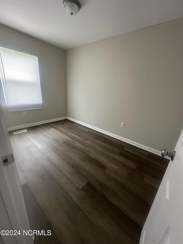 spare room featuring dark wood finished floors, visible vents, and baseboards