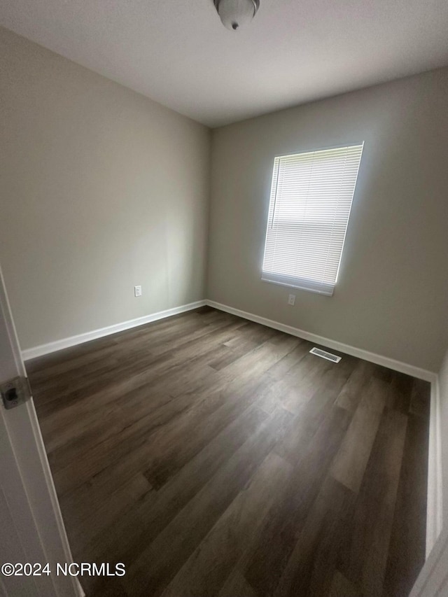 empty room with dark wood-style floors, visible vents, and baseboards