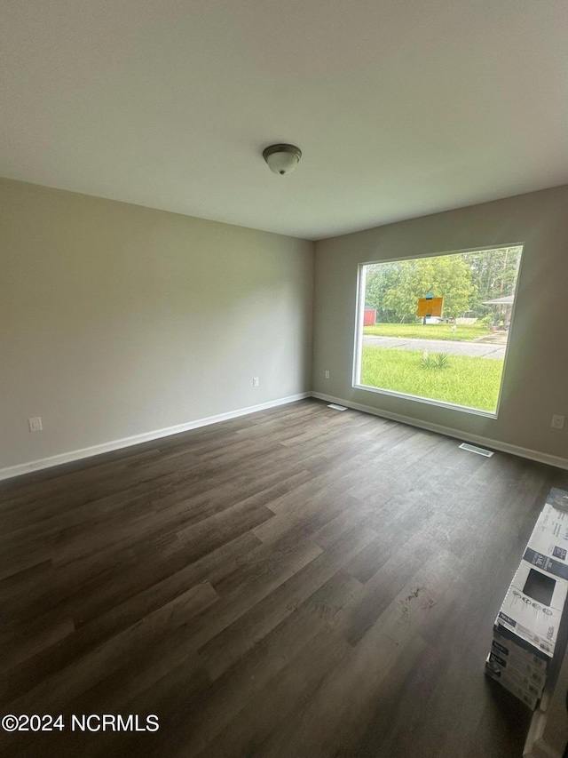 unfurnished room featuring dark wood-style floors, visible vents, and baseboards