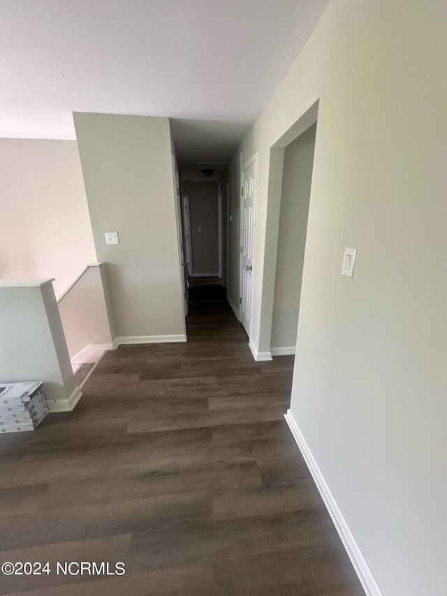 hall with dark wood-style flooring, an upstairs landing, and baseboards