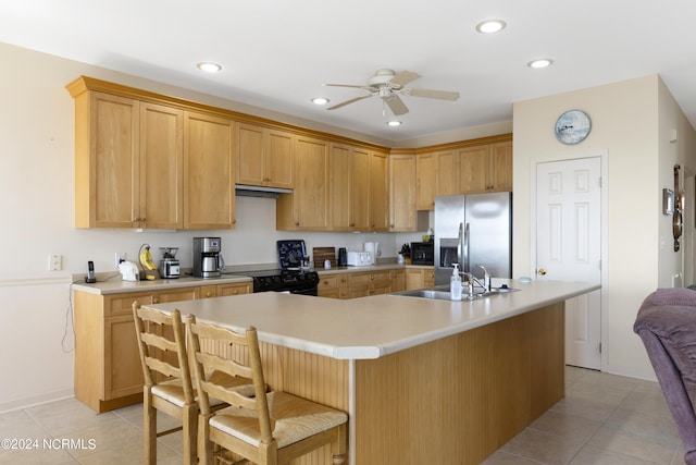 kitchen with gas stove, sink, stainless steel fridge, an island with sink, and light tile patterned floors