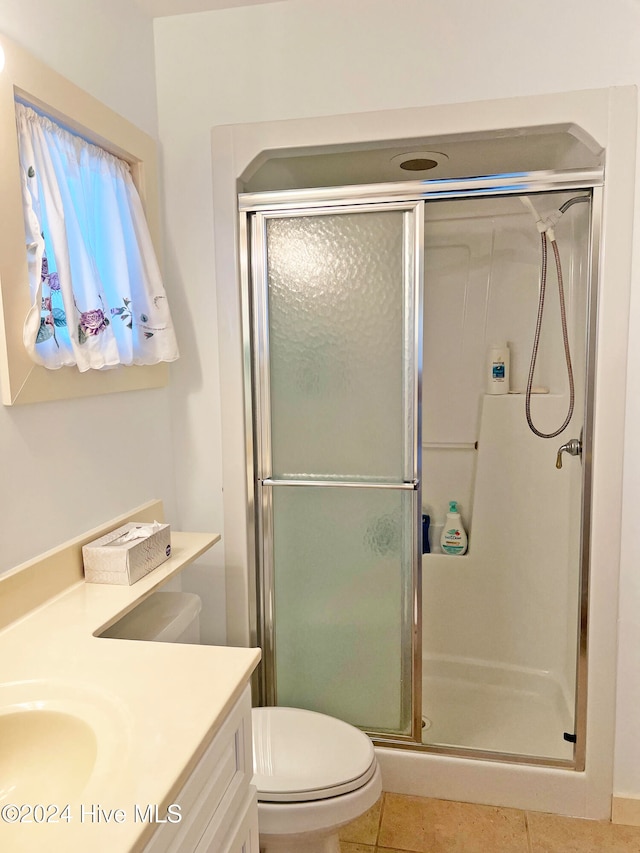 bathroom with tile patterned floors, a shower with door, vanity, and toilet