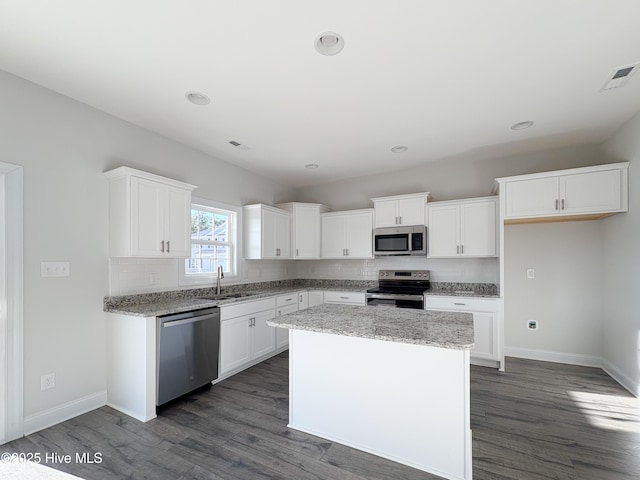 kitchen with a kitchen island, appliances with stainless steel finishes, white cabinetry, sink, and dark wood-type flooring