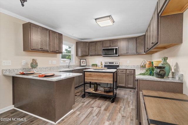 kitchen featuring kitchen peninsula, light stone counters, sink, hardwood / wood-style flooring, and ornamental molding