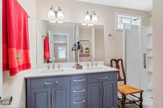 bathroom featuring a shower with door, vanity with extensive cabinet space, and double sink