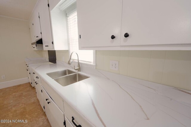 kitchen with light stone counters, white cabinetry, ornamental molding, and sink