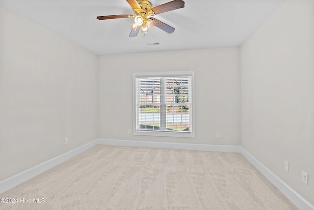 spare room featuring light carpet, a ceiling fan, and baseboards