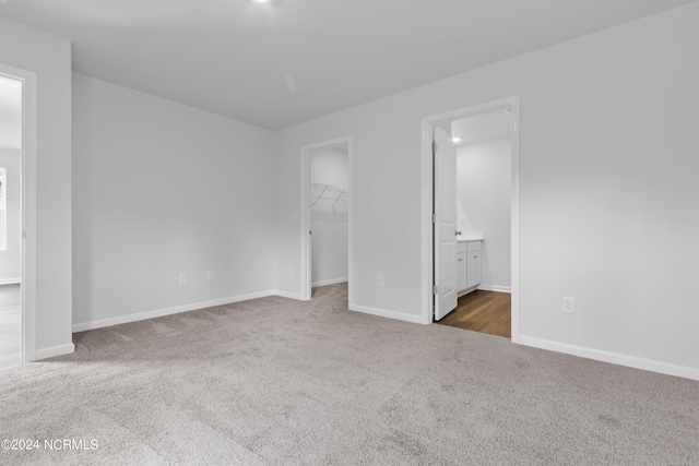 unfurnished bedroom with ensuite bathroom, a closet, a spacious closet, and dark colored carpet