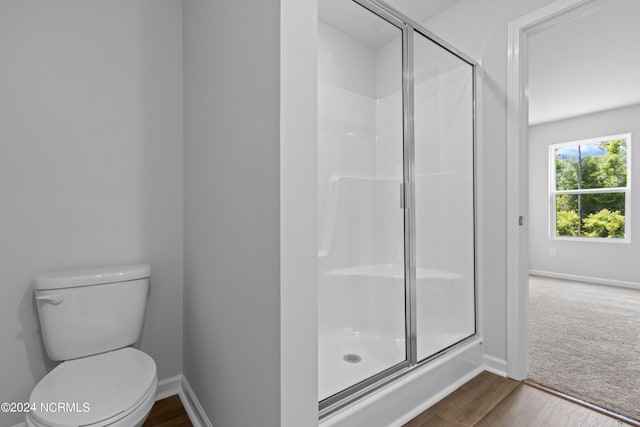 bathroom with hardwood / wood-style floors, a shower with shower door, and toilet