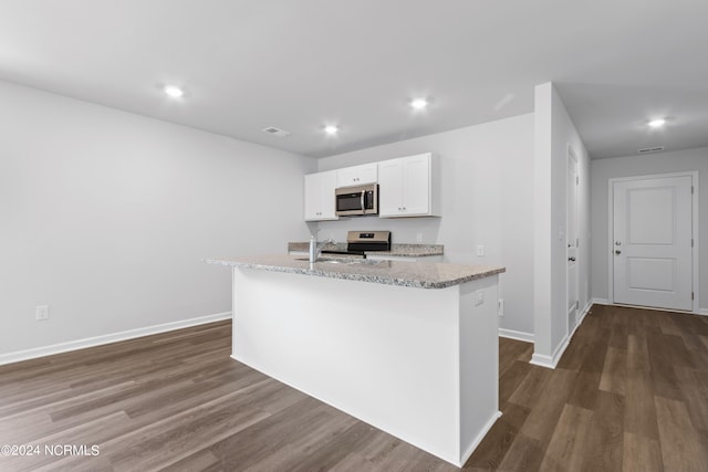 kitchen with appliances with stainless steel finishes, light stone counters, dark wood-type flooring, white cabinets, and an island with sink