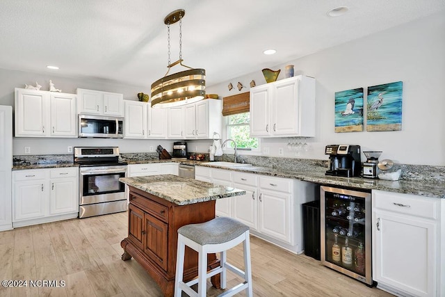 kitchen featuring wine cooler, appliances with stainless steel finishes, white cabinets, a sink, and light wood-type flooring