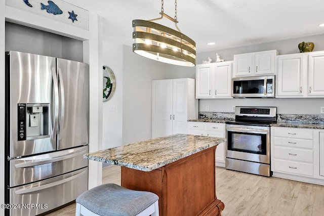 kitchen with white cabinets, light stone counters, a center island, stainless steel appliances, and light wood-style floors