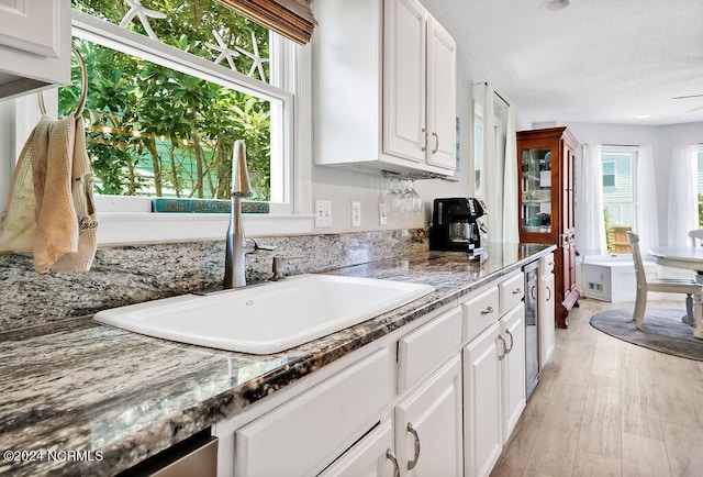 kitchen featuring light stone countertops, light wood finished floors, white cabinetry, and a sink