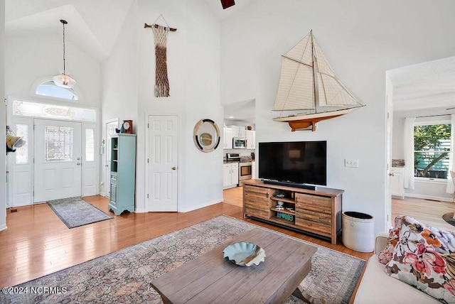 living area featuring high vaulted ceiling, light wood-style flooring, and baseboards