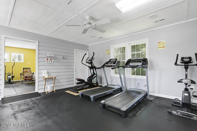 gym featuring wooden walls, visible vents, baseboards, ceiling fan, and ornamental molding