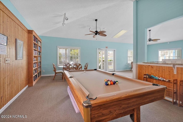 recreation room with lofted ceiling, a healthy amount of sunlight, wooden walls, and a textured ceiling