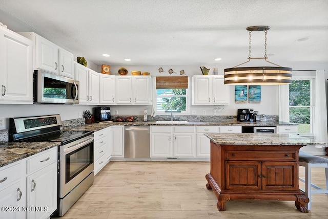 kitchen with stainless steel appliances, light wood finished floors, a sink, and white cabinetry