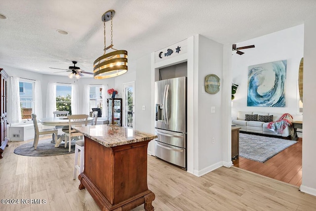 kitchen with a center island, light wood-style flooring, open floor plan, light stone countertops, and stainless steel fridge