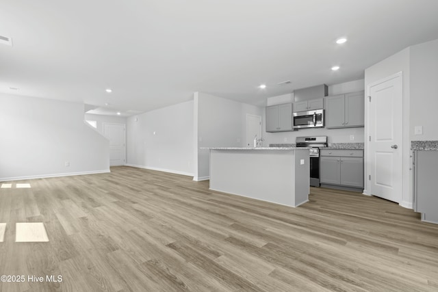 kitchen with gray cabinets, a center island with sink, stainless steel appliances, and light hardwood / wood-style floors