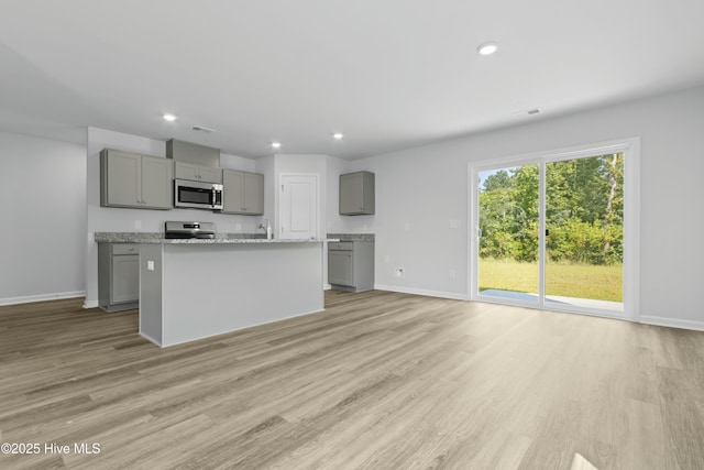 kitchen with light hardwood / wood-style flooring, gray cabinets, light stone countertops, an island with sink, and range