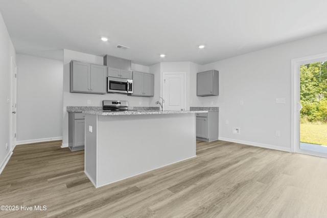 kitchen with range, gray cabinets, light stone counters, and a kitchen island with sink