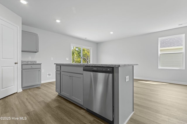 kitchen featuring stainless steel dishwasher, gray cabinetry, sink, a center island with sink, and light hardwood / wood-style flooring